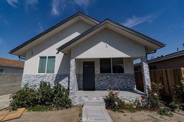 bungalow-style home with covered porch, fence, stone siding, and stucco siding