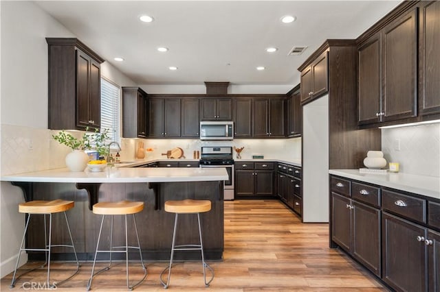 kitchen featuring dark brown cabinetry, visible vents, light wood-type flooring, stainless steel appliances, and recessed lighting