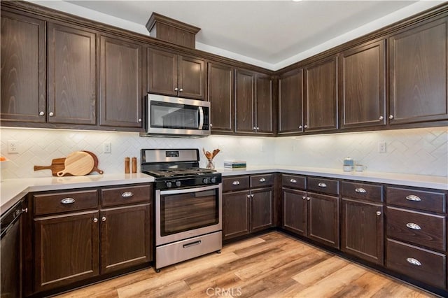 kitchen with dark brown cabinets, light countertops, stainless steel appliances, light wood-type flooring, and backsplash