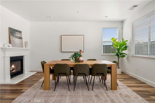 dining room featuring baseboards, visible vents, a glass covered fireplace, and wood finished floors