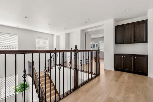 hallway with baseboards, recessed lighting, light wood-style flooring, and an upstairs landing