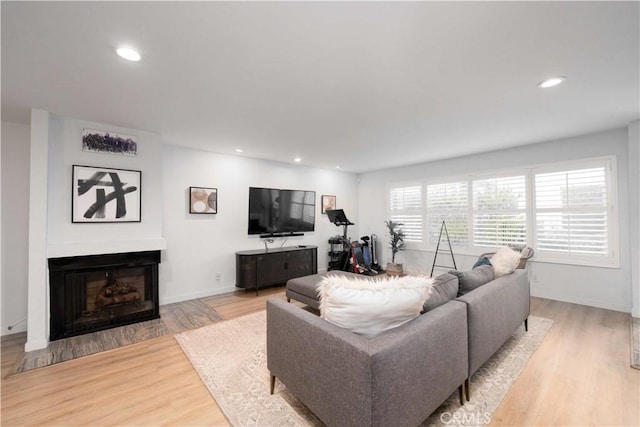 living room featuring recessed lighting, a fireplace with flush hearth, baseboards, and light wood-type flooring