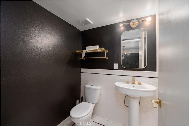 half bathroom featuring wainscoting, tile patterned flooring, toilet, tile walls, and visible vents