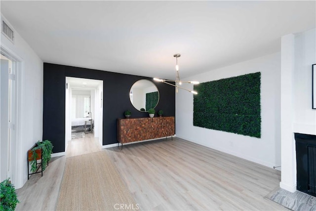 unfurnished living room featuring visible vents, a fireplace, baseboards, light wood-type flooring, and a chandelier