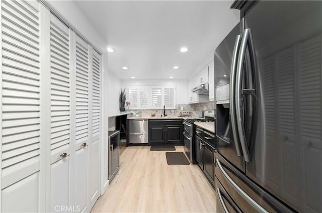 kitchen with light wood-style floors, light countertops, under cabinet range hood, a sink, and appliances with stainless steel finishes