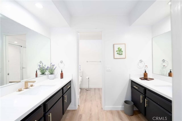 full bath with baseboards, a sink, wood finished floors, and two vanities