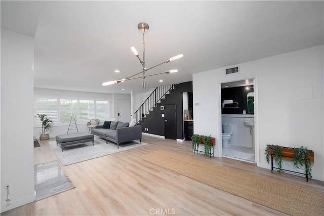 living area featuring visible vents, wood finished floors, a chandelier, and stairway