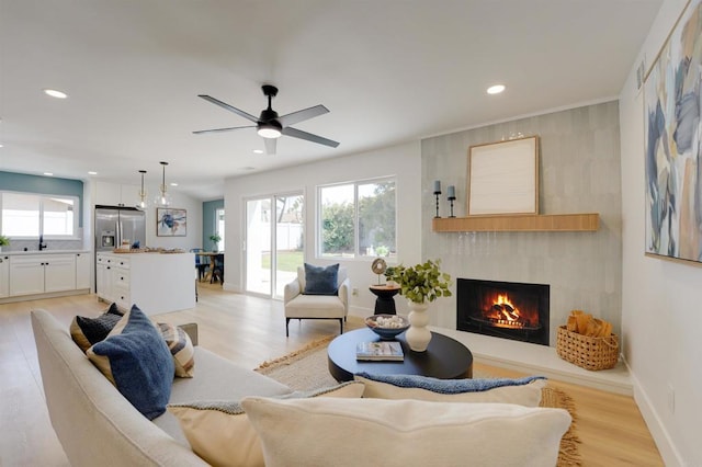 living room featuring a ceiling fan, a large fireplace, baseboards, recessed lighting, and light wood-style flooring