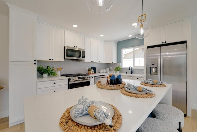 kitchen with decorative backsplash, appliances with stainless steel finishes, hanging light fixtures, a center island, and white cabinets