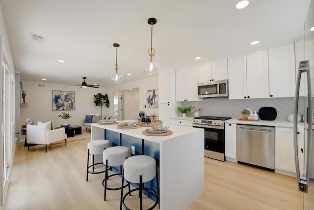 kitchen with visible vents, light wood-style floors, a kitchen bar, white cabinets, and appliances with stainless steel finishes