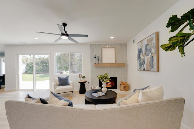 living room featuring light wood finished floors, a large fireplace, recessed lighting, a ceiling fan, and baseboards