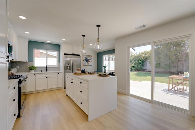 kitchen with appliances with stainless steel finishes, white cabinetry, light wood-type flooring, tasteful backsplash, and visible vents