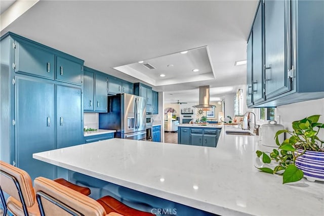 kitchen with blue cabinets, appliances with stainless steel finishes, a sink, a raised ceiling, and a peninsula