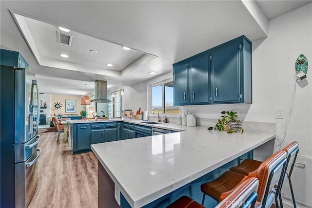 kitchen with light wood-style floors, blue cabinetry, a sink, a peninsula, and stainless steel fridge