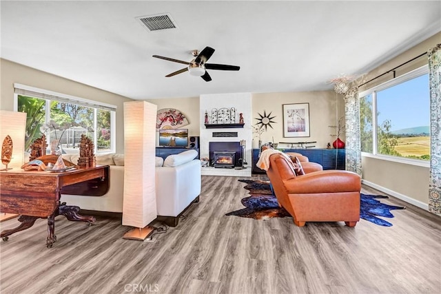 living area featuring visible vents, a glass covered fireplace, wood finished floors, baseboards, and ceiling fan
