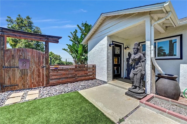 property entrance featuring fence, a gate, and stucco siding