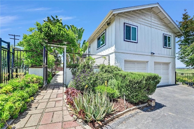 view of side of property with fence, a garage, board and batten siding, stucco siding, and driveway