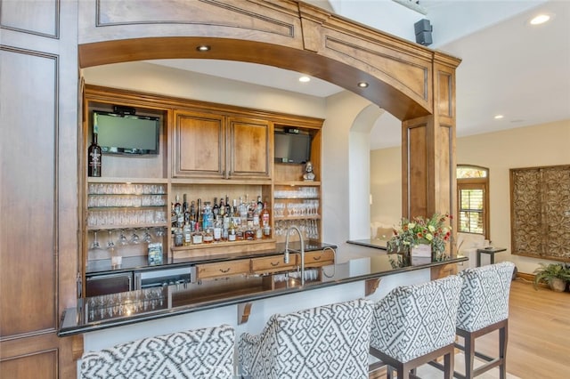 bar with wet bar, arched walkways, a sink, light wood-style floors, and recessed lighting