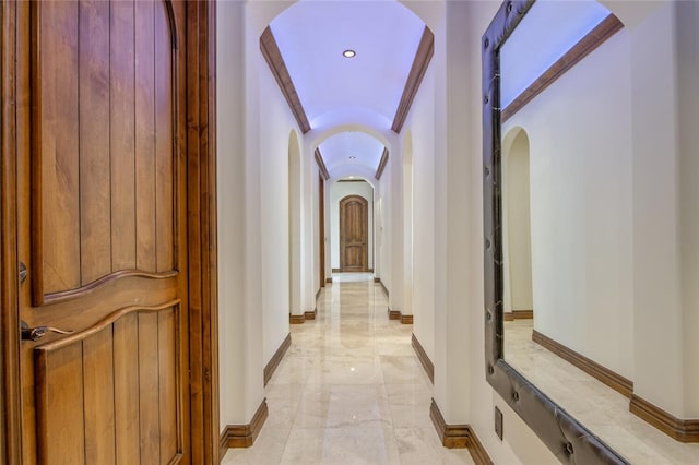 hallway with arched walkways, baseboards, and marble finish floor