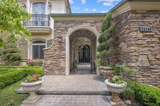 doorway to property with french doors, stone siding, stucco siding, and a balcony