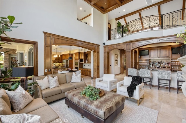 living area featuring arched walkways, a towering ceiling, beam ceiling, and bar area