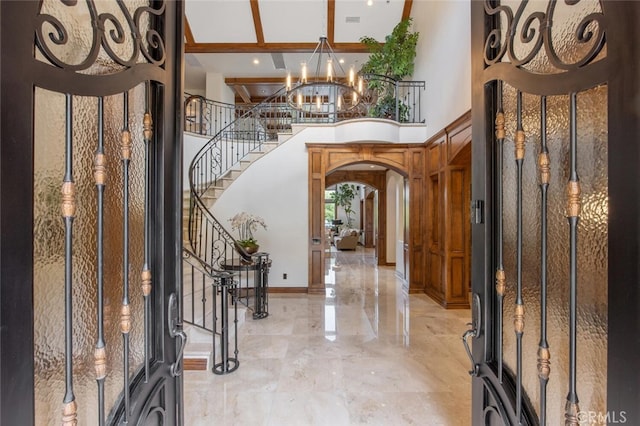 foyer featuring a high ceiling, arched walkways, a chandelier, marble finish floor, and stairs