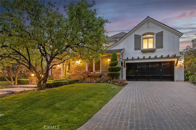 view of front facade featuring decorative driveway, an attached garage, a front lawn, and stucco siding