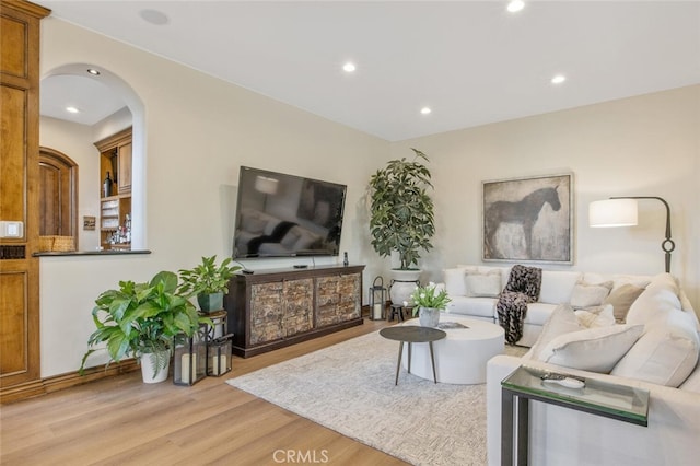 living area with recessed lighting, arched walkways, and light wood finished floors