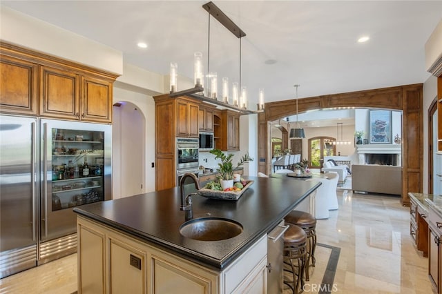 kitchen with pendant lighting, a sink, built in appliances, dark countertops, and arched walkways