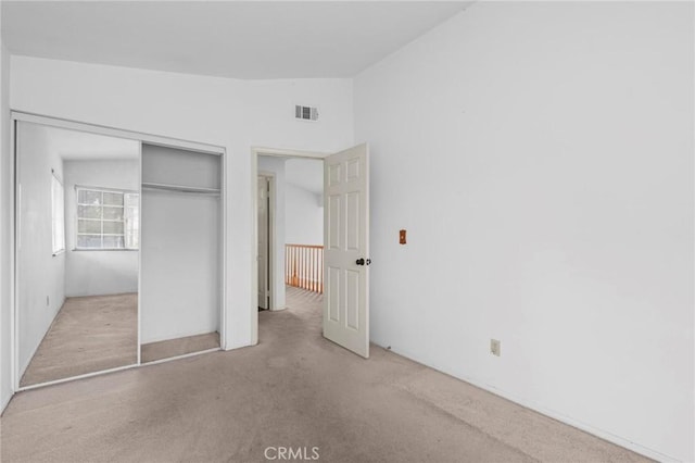 unfurnished bedroom with a closet, carpet floors, lofted ceiling, and visible vents