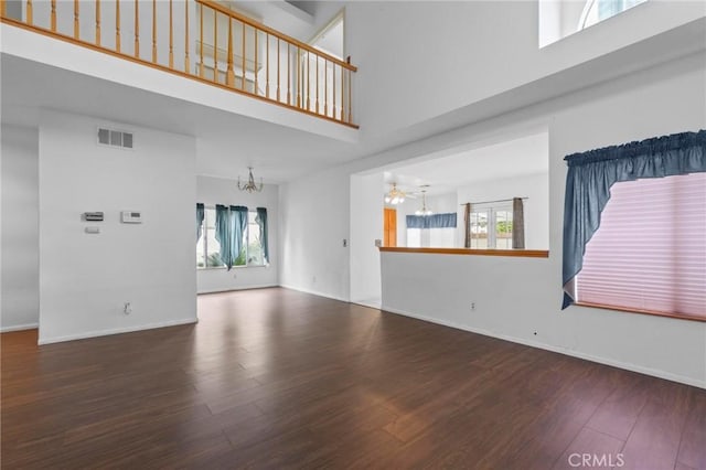 unfurnished living room with visible vents, wood finished floors, baseboards, a chandelier, and a high ceiling