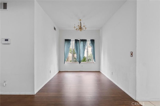 empty room with visible vents, baseboards, wood finished floors, and a chandelier