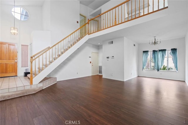 unfurnished living room featuring a notable chandelier, stairs, wood finished floors, a towering ceiling, and visible vents