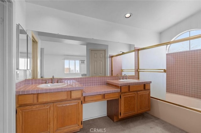 bathroom featuring a sink, bath / shower combo with glass door, and double vanity