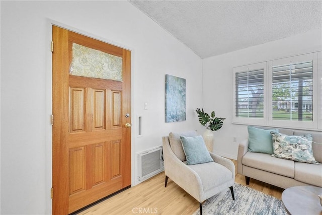 sitting room with visible vents, a textured ceiling, light wood finished floors, and vaulted ceiling