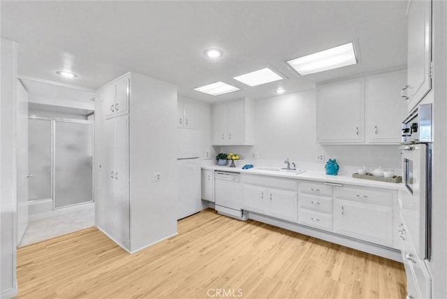 kitchen featuring light wood-style floors, a sink, white cabinets, and white appliances