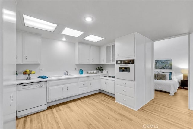 kitchen featuring white appliances, light countertops, white cabinets, a sink, and light wood-style flooring