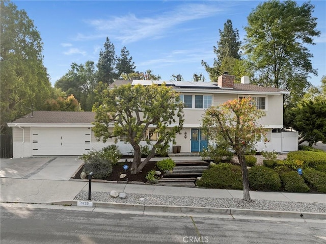 view of front of property with a garage, solar panels, a chimney, and concrete driveway