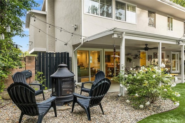 back of property featuring a ceiling fan, fence, a fire pit, and stucco siding