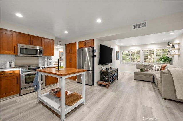 kitchen with brown cabinets, appliances with stainless steel finishes, light countertops, light wood-style flooring, and recessed lighting