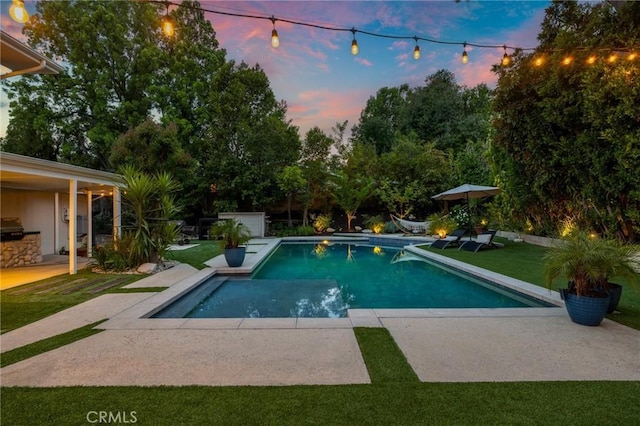 pool at dusk featuring a patio area, an outdoor pool, and a yard