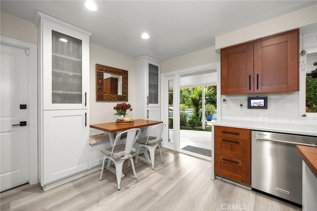 kitchen with light wood finished floors, light countertops, tasteful backsplash, stainless steel dishwasher, and glass insert cabinets