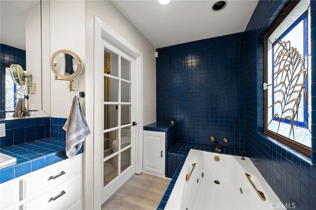 full bathroom with a tub with jets, decorative backsplash, and wood finished floors