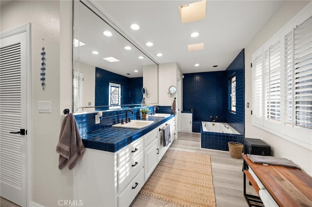 full bath with a garden tub, a sink, wood finished floors, and double vanity