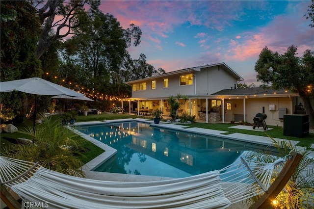 pool at dusk with a yard, a patio, and an outdoor pool