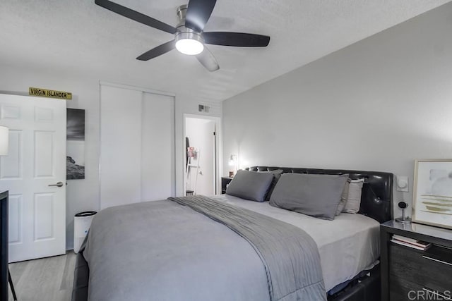 bedroom with ceiling fan, a textured ceiling, wood finished floors, visible vents, and a closet