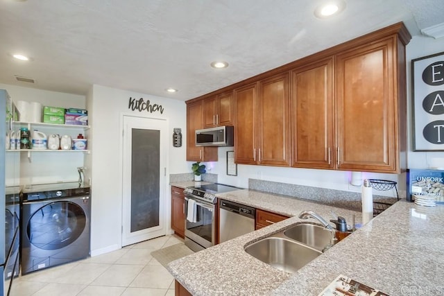 kitchen featuring brown cabinets, a sink, light tile patterned floors, stainless steel appliances, and washer and clothes dryer