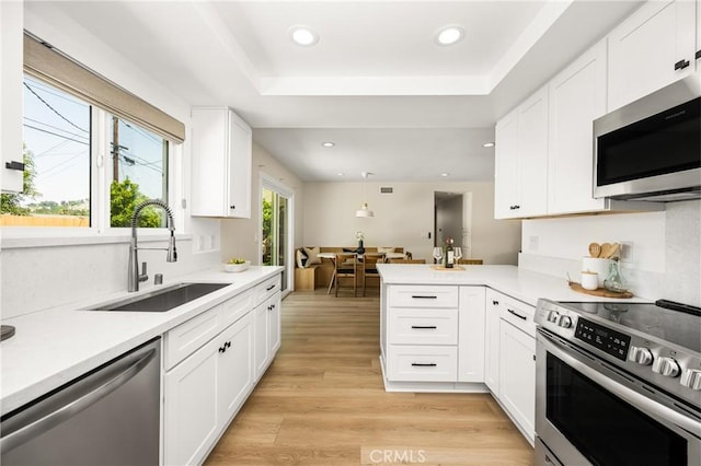 kitchen featuring appliances with stainless steel finishes, a sink, light countertops, white cabinets, and a peninsula