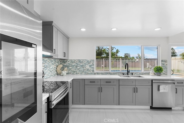 kitchen with stainless steel appliances, gray cabinetry, decorative backsplash, and a sink