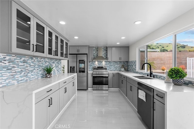 kitchen featuring a sink, wall chimney exhaust hood, stainless steel appliances, decorative backsplash, and gray cabinetry